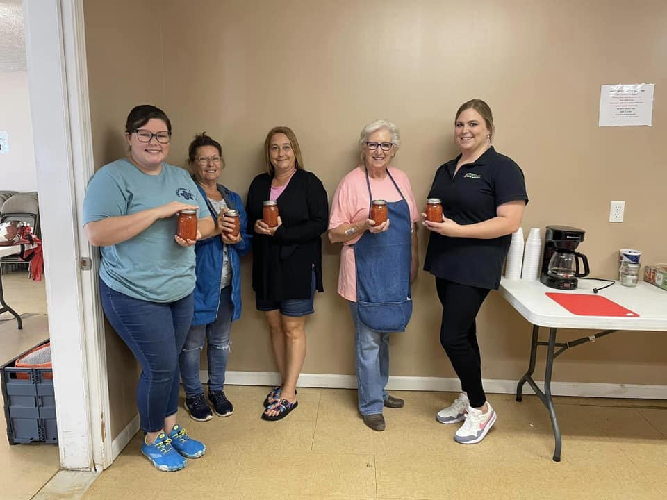 Five women holding canned tomatoes they made in our FCS canning class